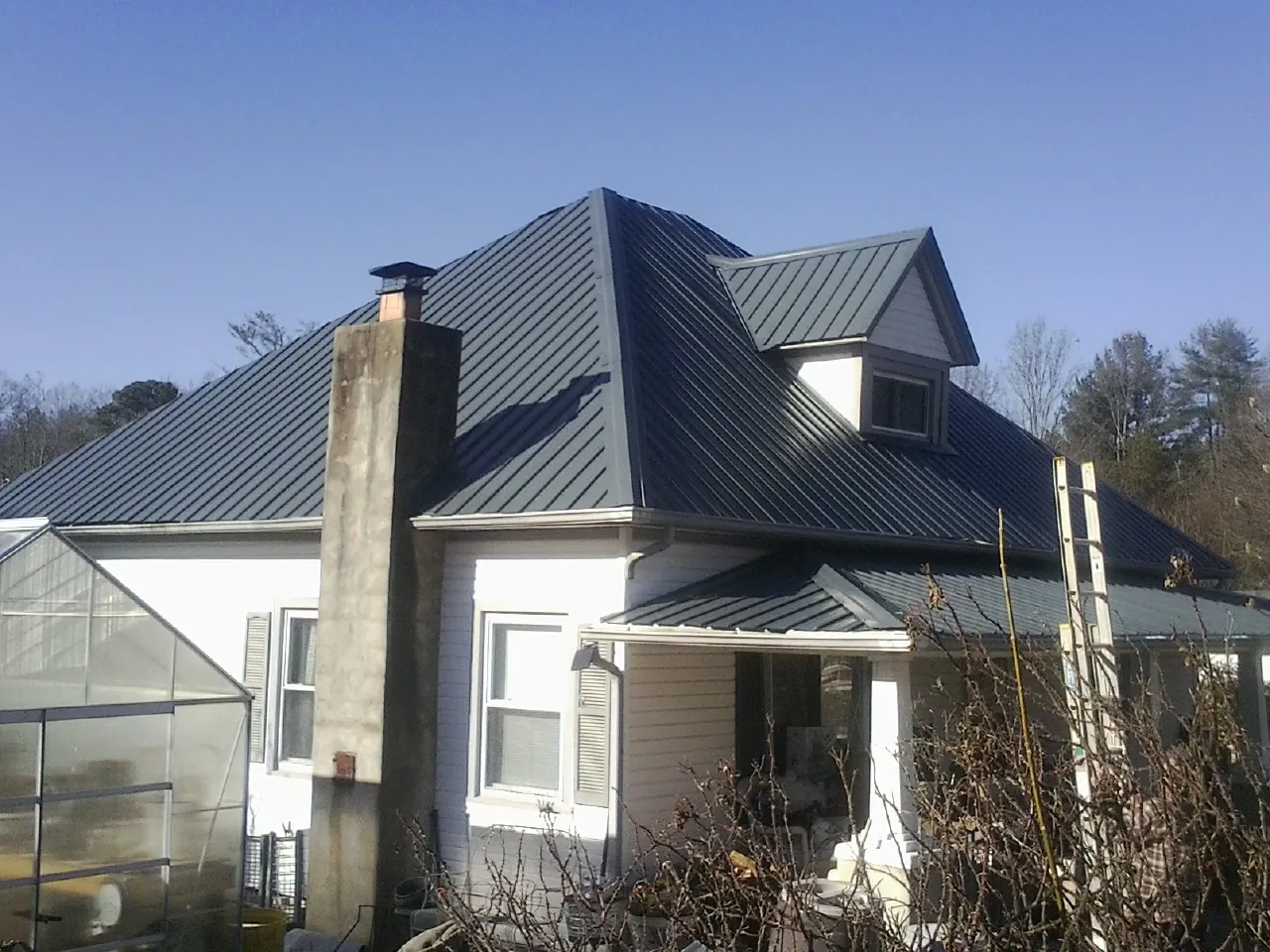 Dark blue standing seam metal roof on a white farmhouse with dormer — Slate & Tile Roof Repair by Roofing Brothers in Jermyn