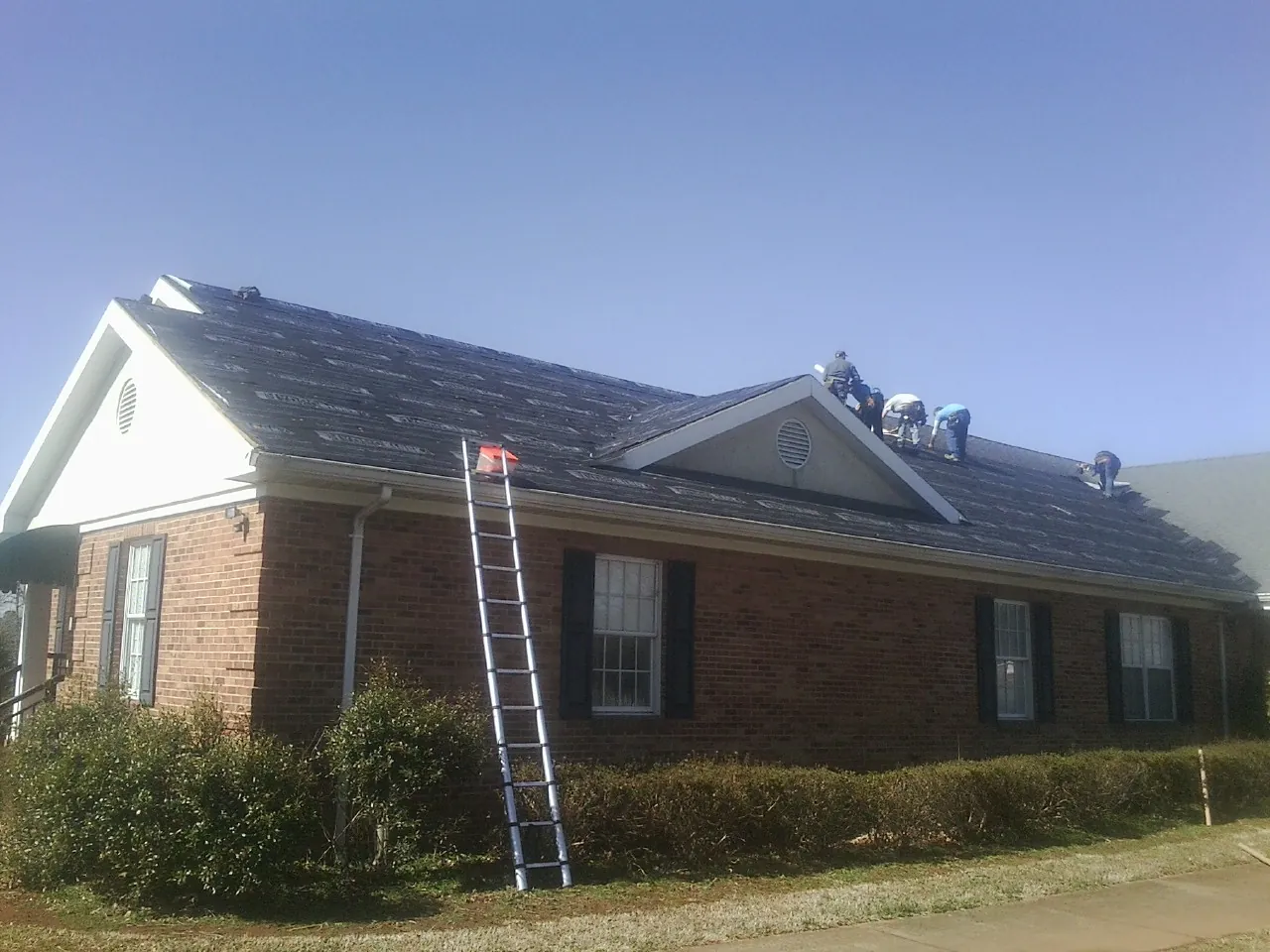 Crew tearing shingles off a brick ranch roof with a ladder set — Emergency Roof Repair work by our crew in Jermyn