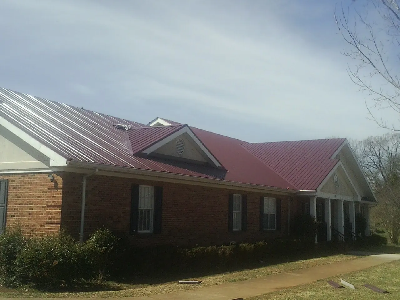 Red metal roof with gabled entries on a long brick building, from a Hail Damage Roof Repair job in Jermyn