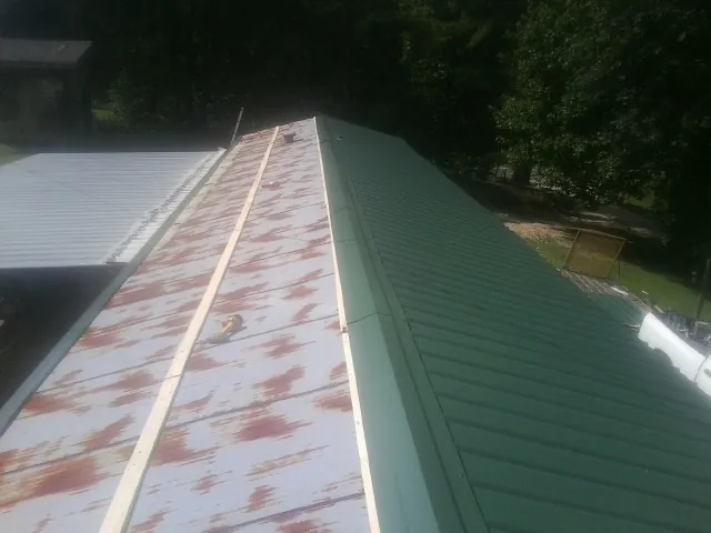 Old rusted panels beside newly installed green metal roofing — Wind Damage Roof Repair by Roofing Brothers in Jermyn