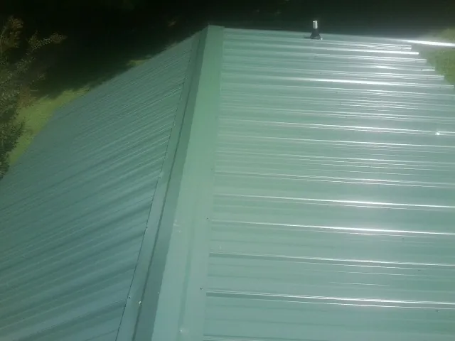 New green metal panels meeting at the ridge of a roof — Flat Roof Repair work by our crew in Jermyn