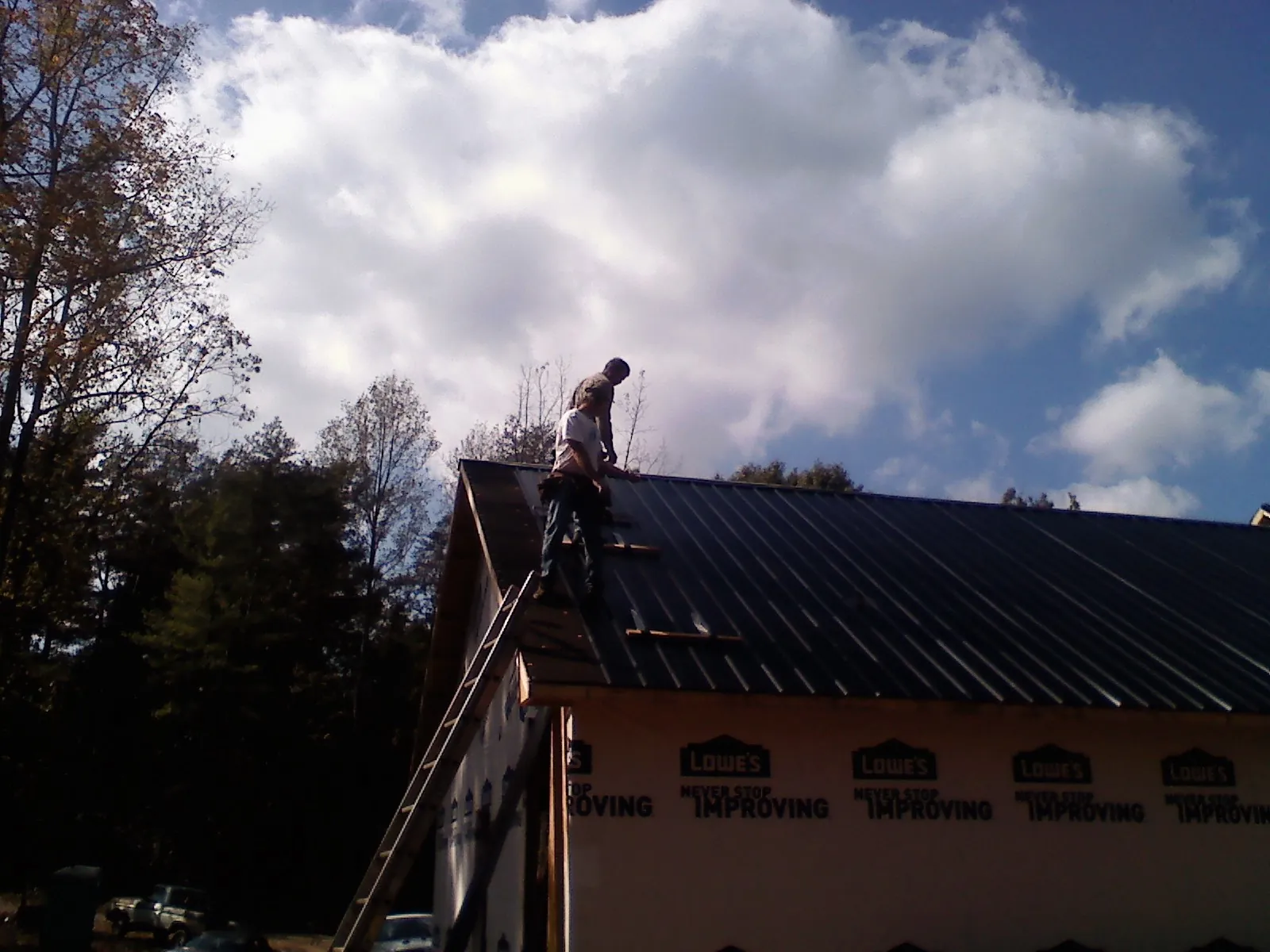 Roofer fastening dark metal panels high against a cloudy sky, from a Roof Inspection job in Jermyn