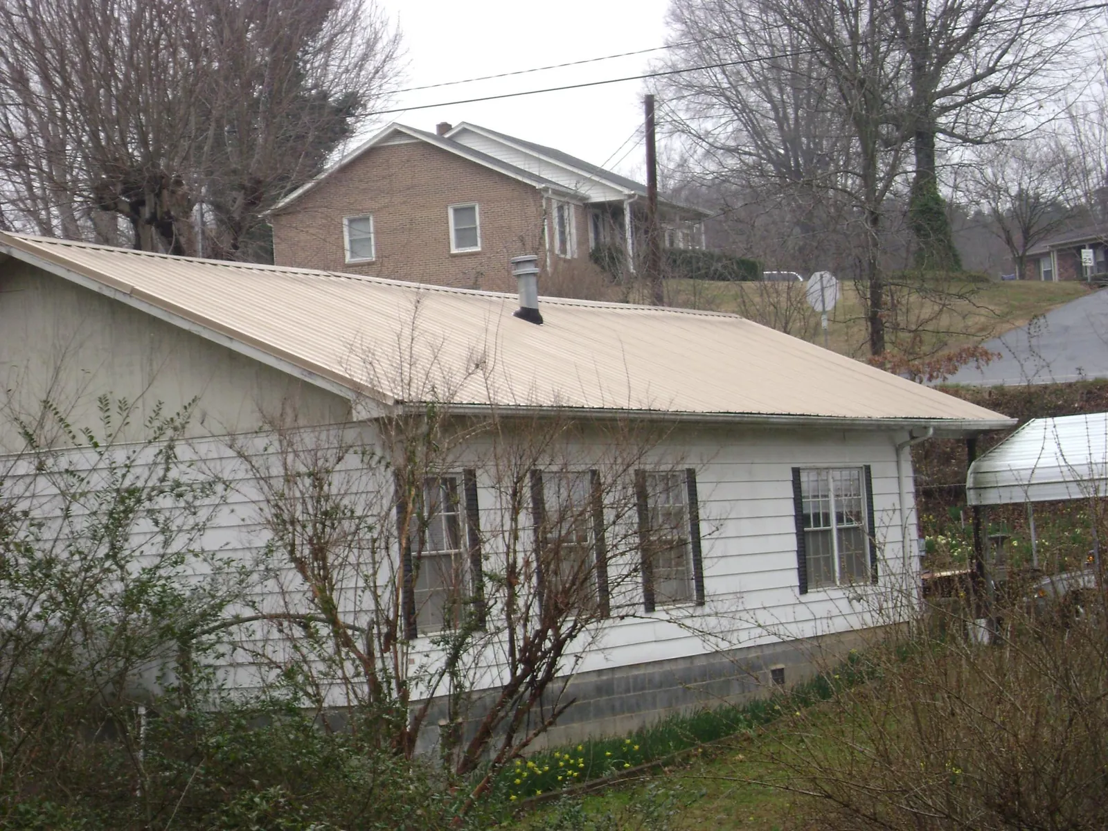 Tan metal roof on a white sided house set into a hillside — Commercial Roofing by Roofing Brothers in Jermyn